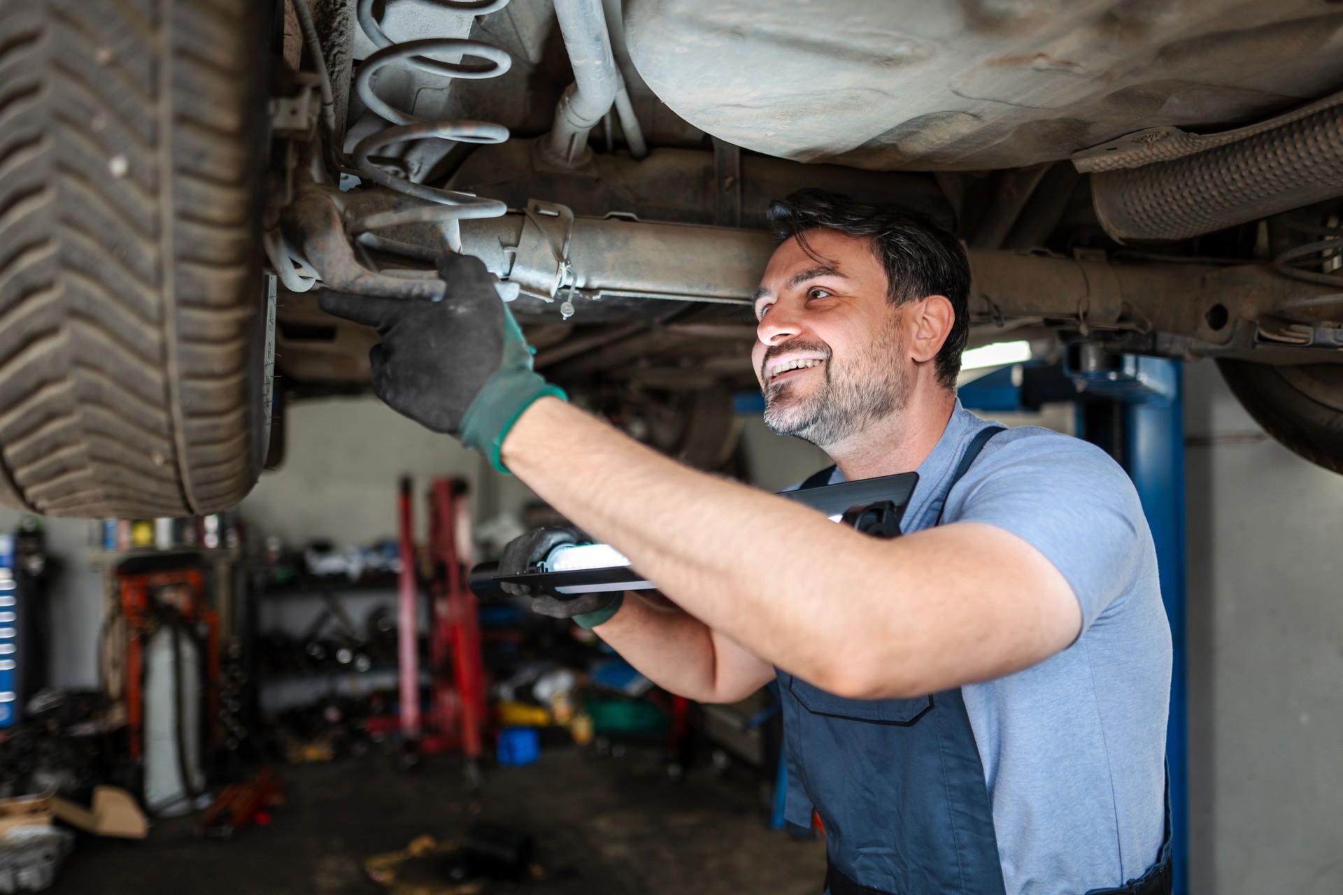 Mechanic inspecting car suspension with led lamp in garage