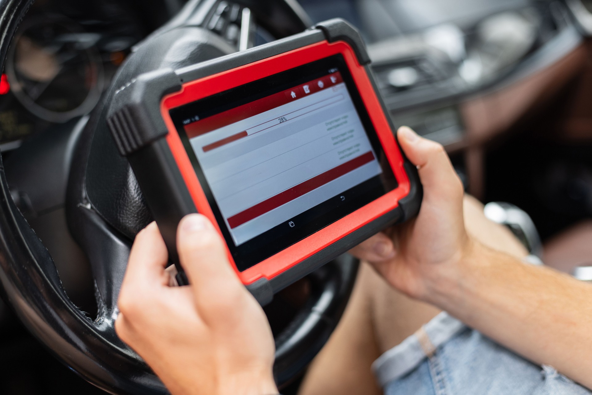 Mechanic using a digital diagnostic scanner to check car systems inside the vehicle. Man holds a modern diagnostic scanner inside a car, checking vehicle systems and electronics. Automotive techn